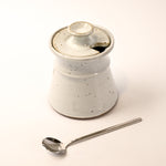 White ceramic container with a lid and a silver spoon on a light background