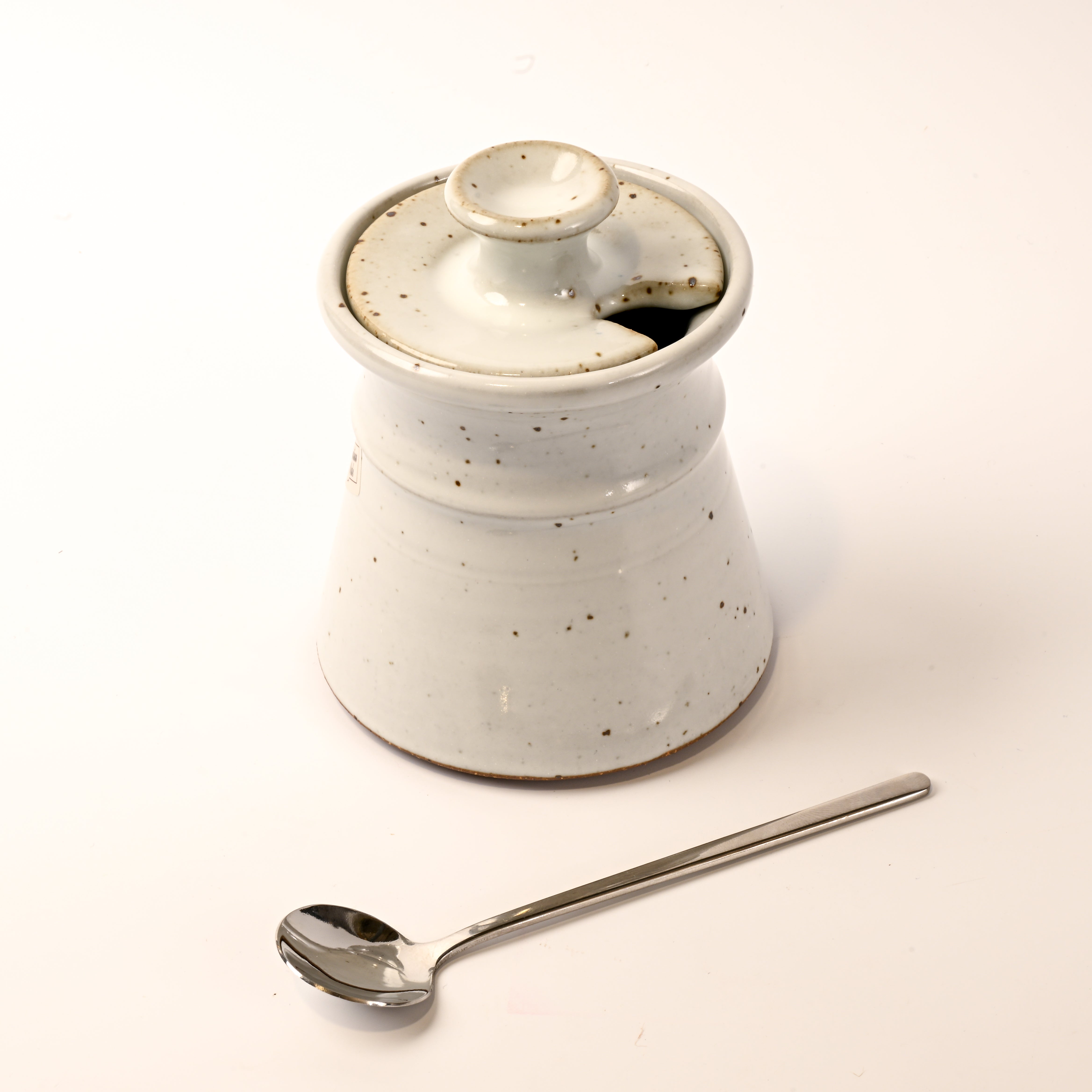 White ceramic container with a lid and a silver spoon on a light background
