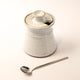 White ceramic container with a lid and a silver spoon on a light background