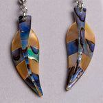 A pair of leaf-shaped dangle earrings made from iridescent abalone shell pieces in blue, gold, and brown tones, hanging from silver-toned rings on a light gray background.