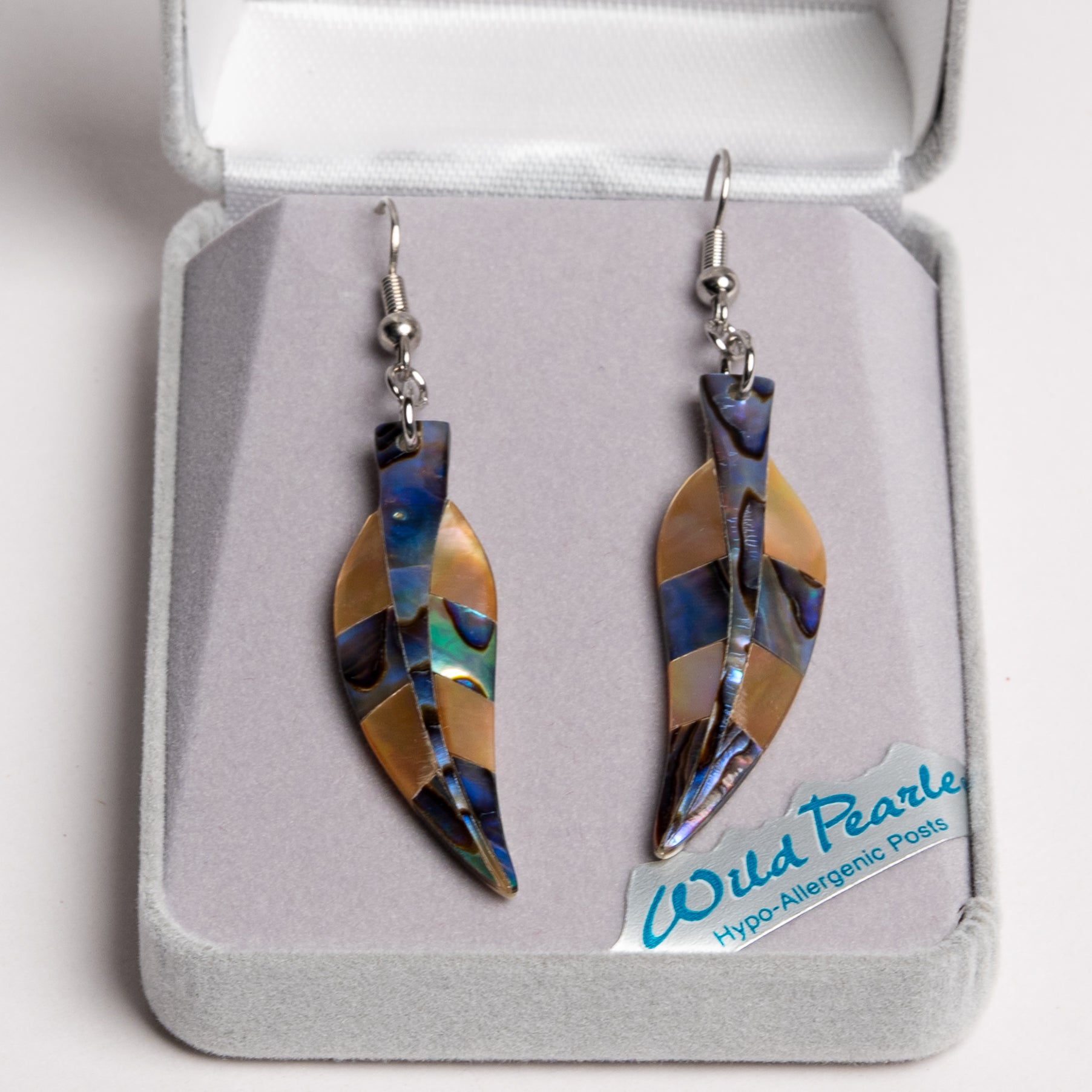 A pair of Wild Pearls hypo-allergenic post earrings displayed in an open gray presentation box. The earrings feature a leaf-shaped design made of iridescent abalone shell pieces showing blue, green, and gold tones, suspended from silver fishhook wires.