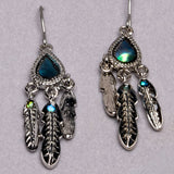 A pair of silver-toned dangle earrings with teardrop-shaped iridescent blue-green stones and three feather charms, including one larger feather with a small green stone, displayed on a light gray textured background.