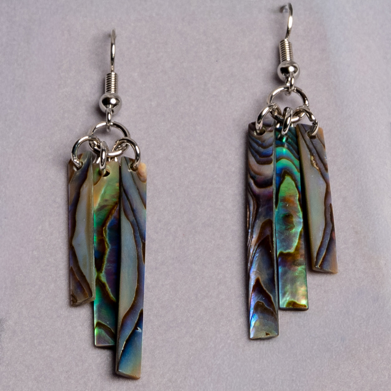 A close up of abalone shell earrings, showing the blue, purple, and green coloring of each earring.
