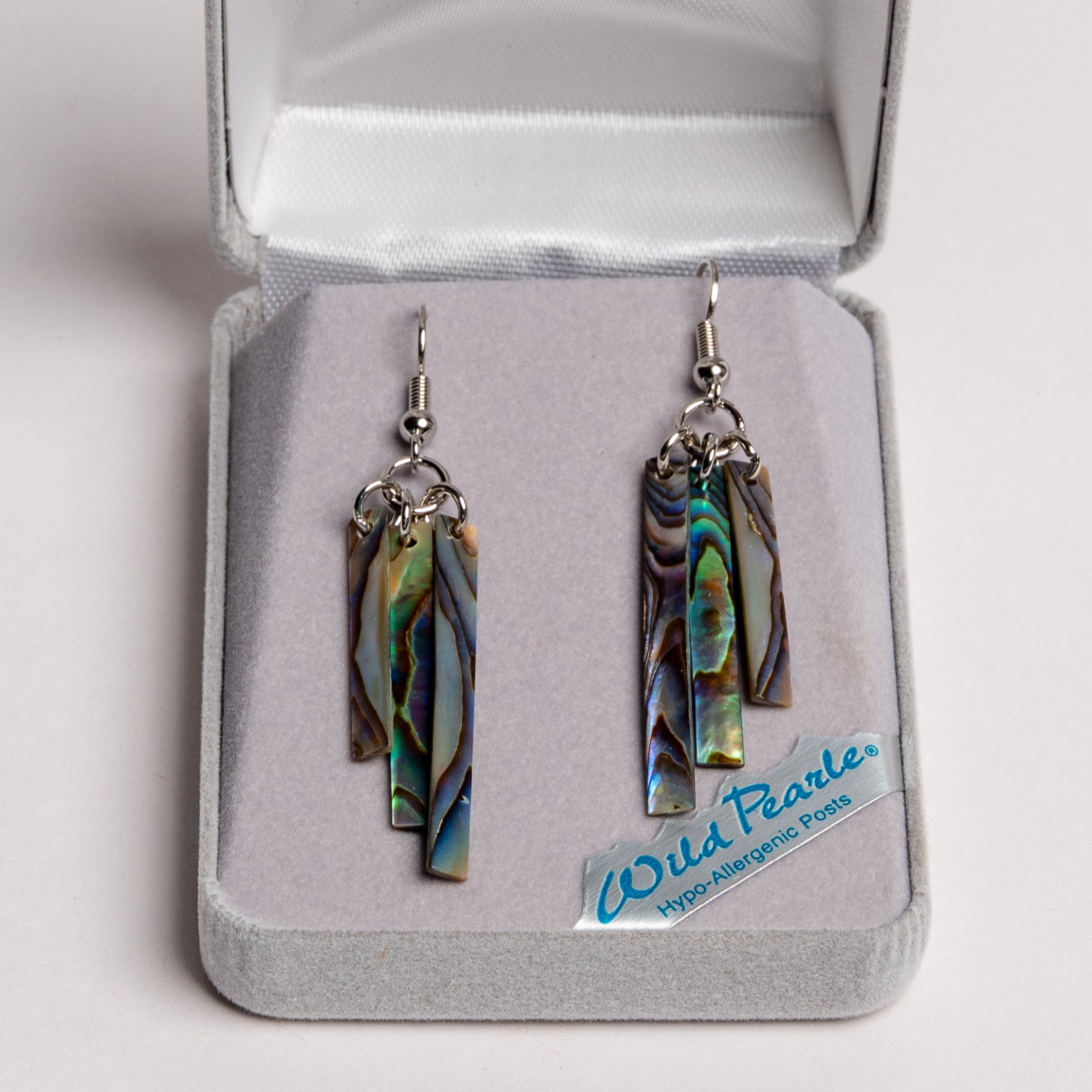A set of abalone shell earrings in the shape of wind chimes set in a grey clamshell box.