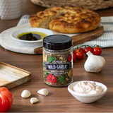 Jar of herbs with wild garlic flavor on a wooden table with bread and vegetables.