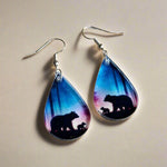 Teardrop-shaped earrings with bear silhouettes on a wooden surface