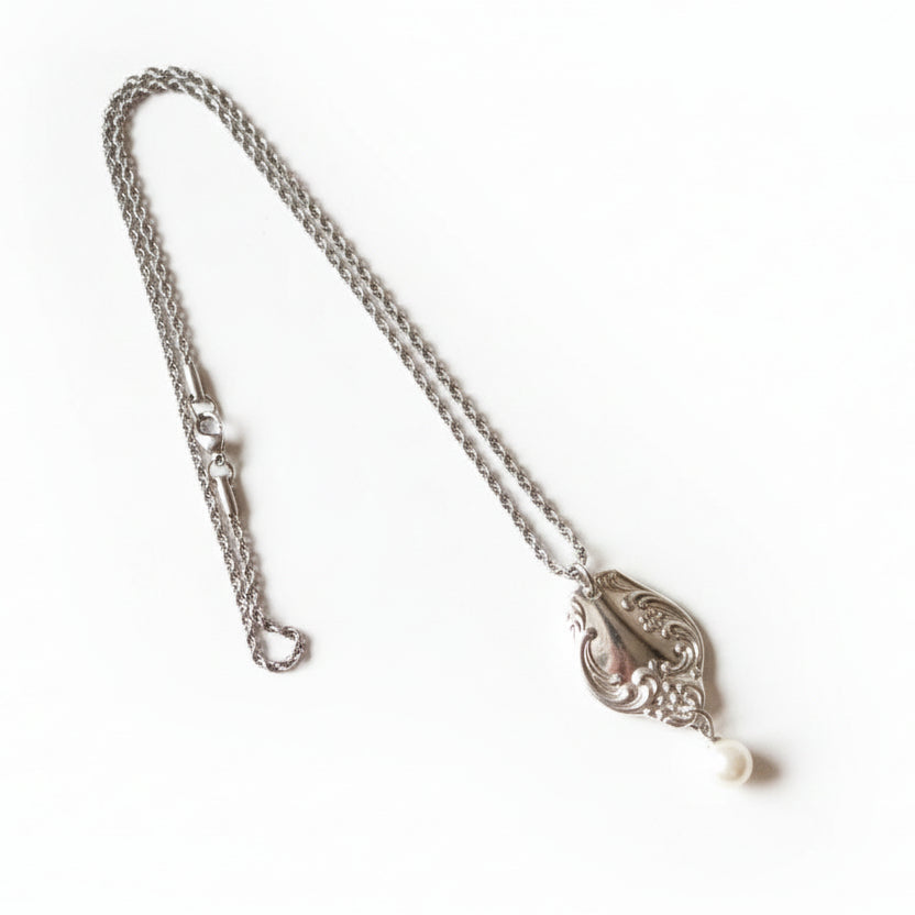 Silver necklace with a pendant on a light wooden floor
