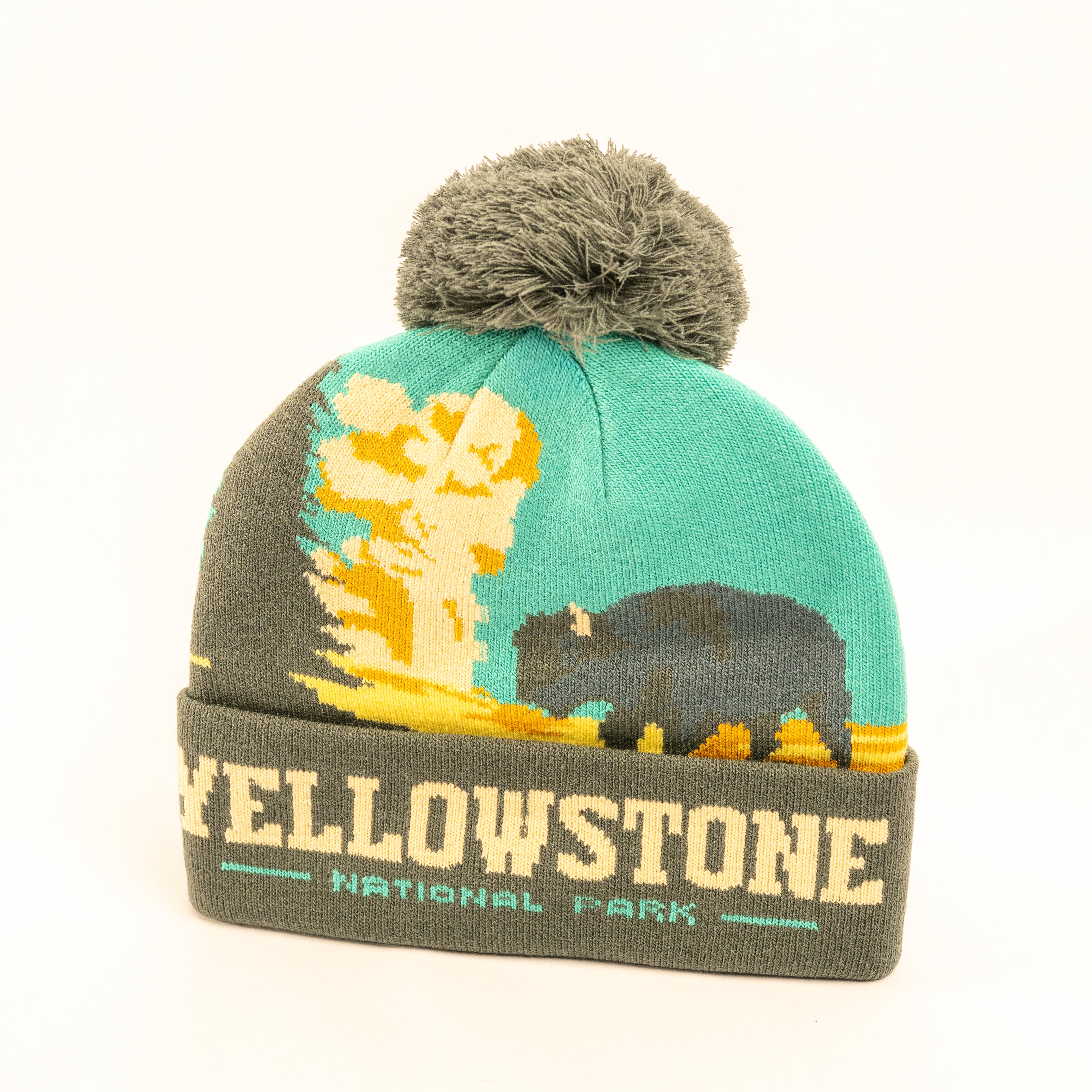 A knit Yellowstone National Park pom-pom beanie featuring a turquoise and olive green design with a bison and mushroom cloud graphic, and a folded cuff reading 'YELLOWSTONE NATIONAL PARK'.