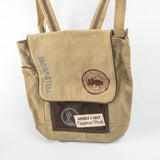 A beige canvas tote bag with dark brown accents, featuring a front pocket with a brown patch that reads 'America's First National Park' and a circular Yellowstone logo, alongside vertical 'Yellowstone' text.