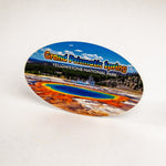 An oval-shaped souvenir sticker featuring a colorful landscape of Grand Prismatic Spring in Yellowstone National Park, displayed on a plain white background.