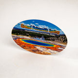 An oval-shaped souvenir sticker featuring a colorful landscape of Grand Prismatic Spring in Yellowstone National Park, displayed on a plain white background.