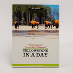 A physical copy of the book 'Yellowstone in a Day' by Yellowstone Forever, standing upright against a neutral light gray background. The cover features a photograph of bison in Yellowstone National Park, with a light gray lower section containing the title and a bright green stripe at the bottom.