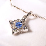 Silver pendant with blue gemstone on a gold chain against a white background