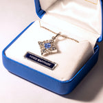 Star-shaped pendant with blue gemstone and gold chain in a jewelry box labeled 'Yogo Sapphire'.