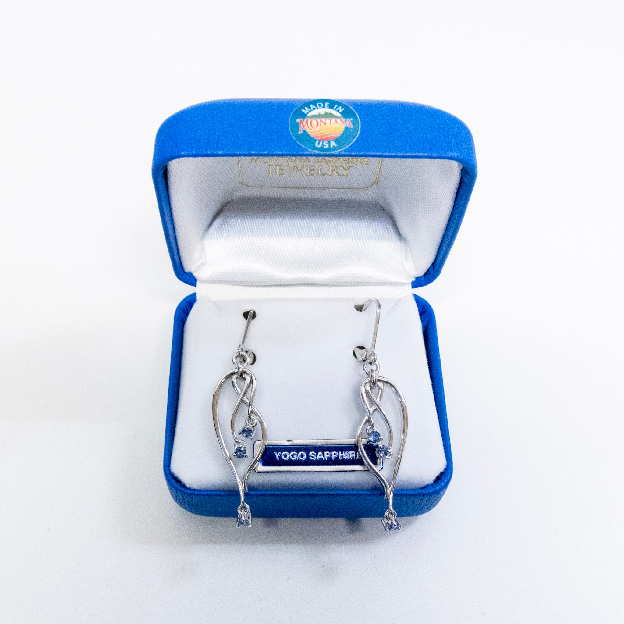 Silver earrings in a blue jewelry box with 'Yogo Sapphires' branding.