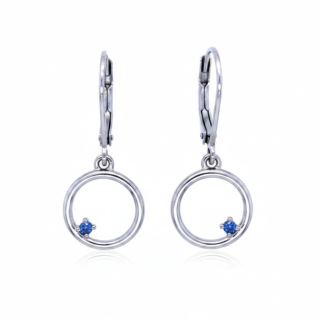 Pair of silver earrings with circular design and blue montana yogo sapphires on a white background