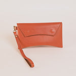 Brick colored leather clutch with a strap on a light beige background