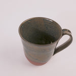 handcrafted mug with a blue and tan glaze that colors half of the piece. the bottom is uncovered. on a white background