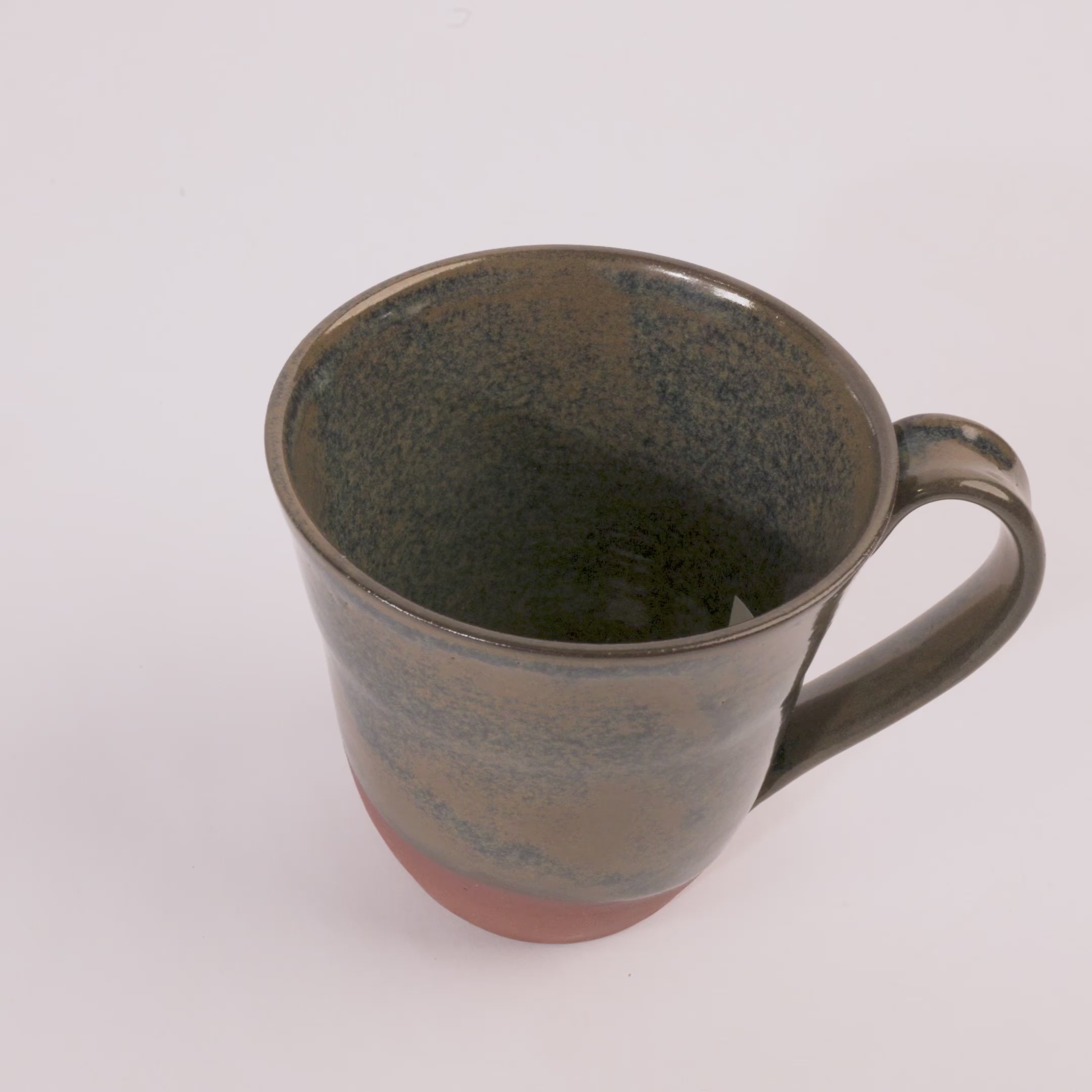 handcrafted mug with a blue and tan glaze that colors half of the piece. the bottom is uncovered. on a white background