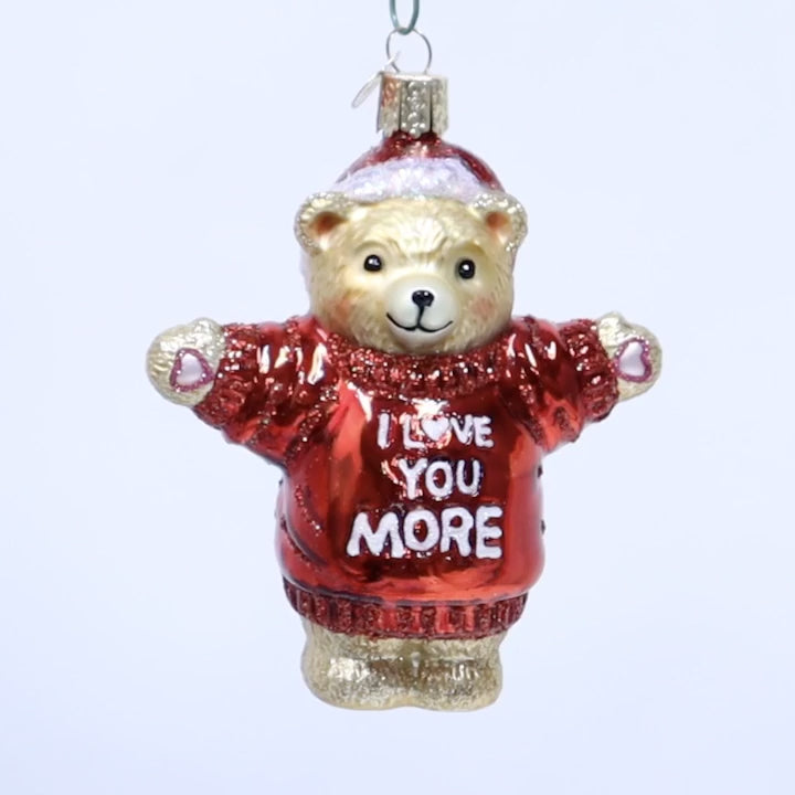 Glass bear ornament wearing a red sweater with 'I love you more' text on a white background