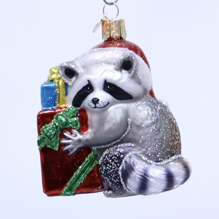 video of a Glass ornament of a raccoon wearing a Santa hat with presents on a white background