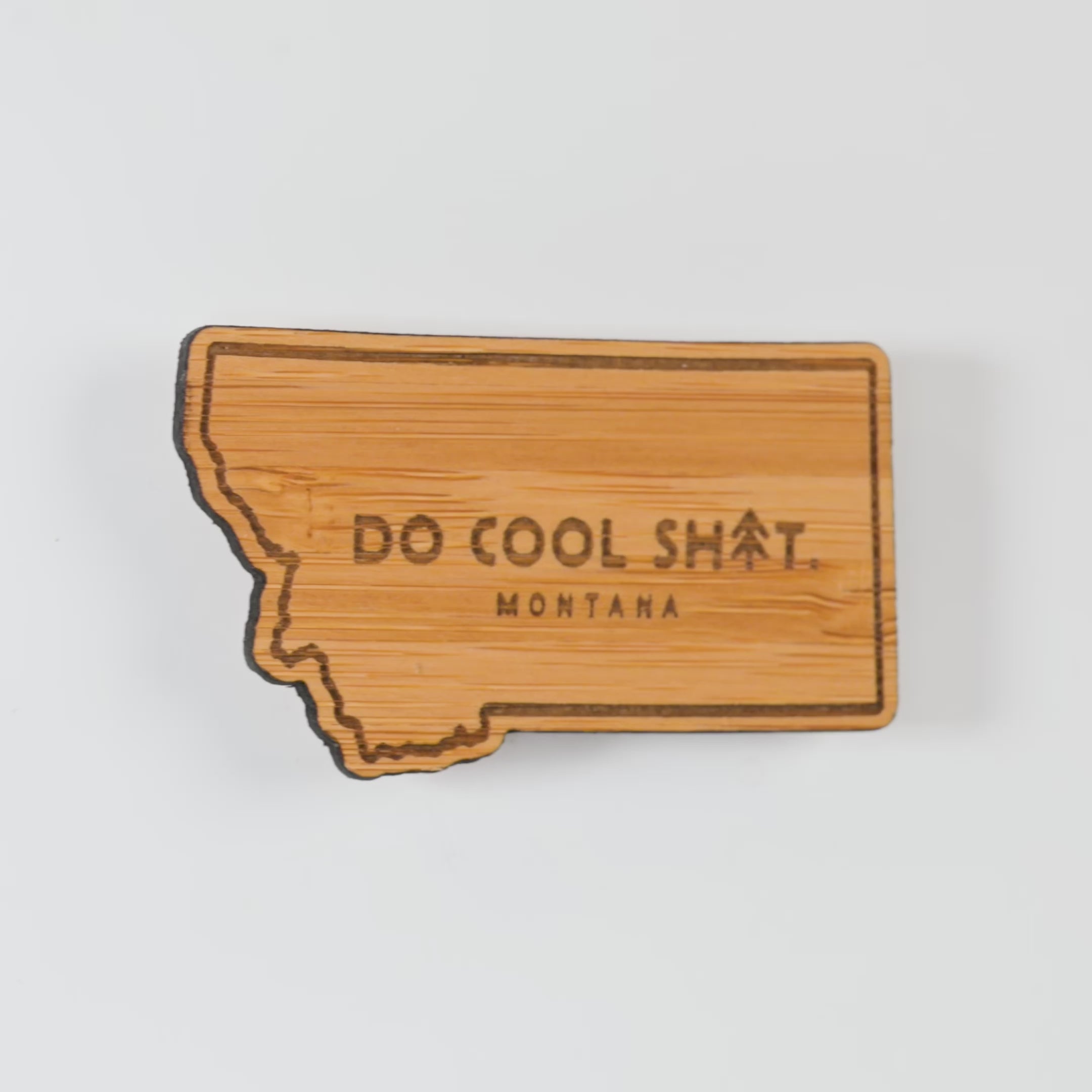 Wooden state-shaped magnet with 'Do Cool Sh*t. Montana' text on a white background
