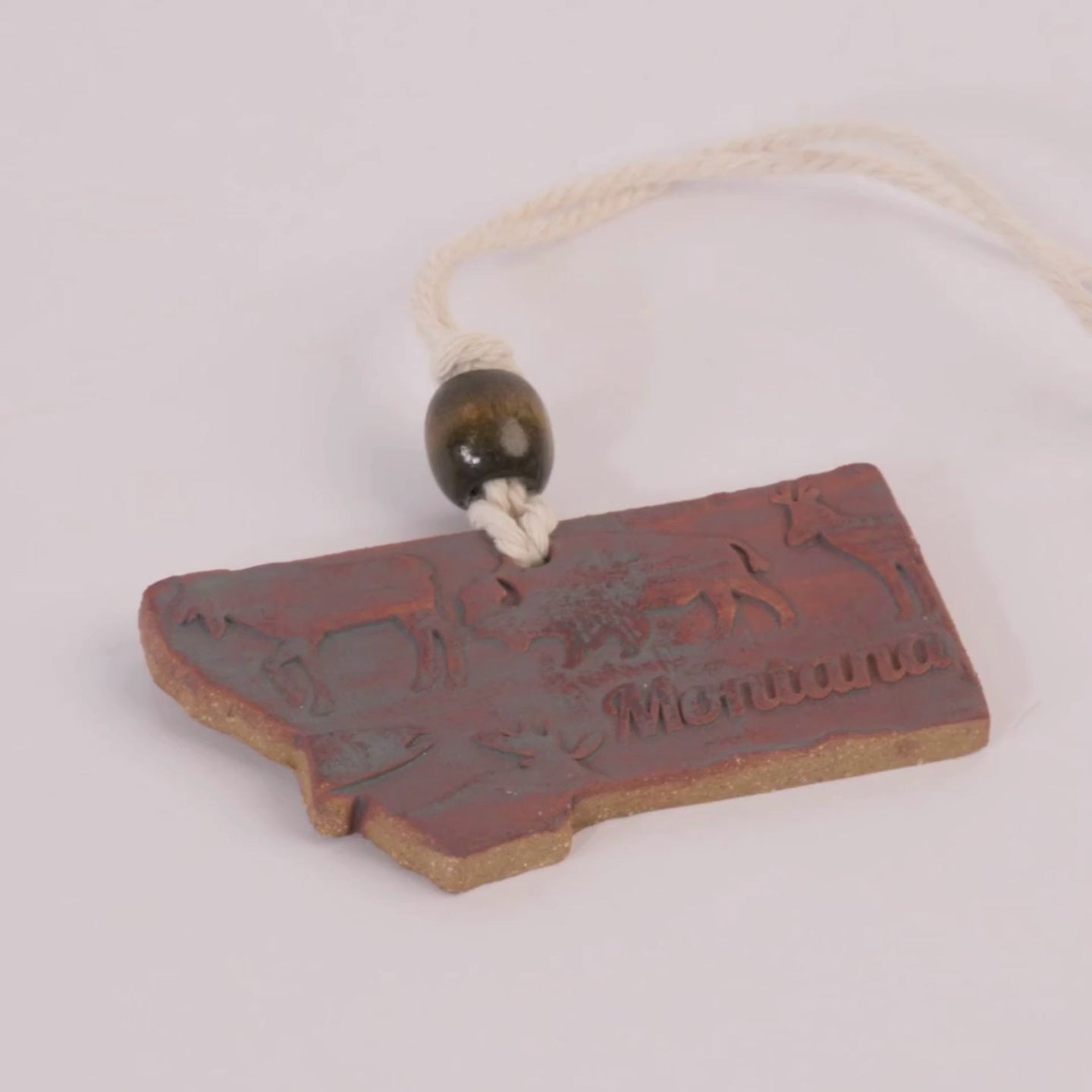 Decorative sign shaped like the state of Montana with animal illustrations and 'Montana' text, hanging on a white background.