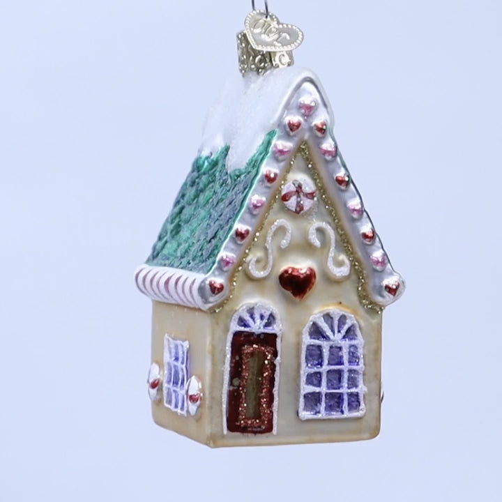 Decorative gingerbread house ornament with a green roof and red door on a white background