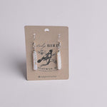 A pair of white pearl dangle earrings on a brown kraft display card with a black bird illustration and the text Lady Bird, Bozeman, MT, Ladybirdmk.com, photographed against a light gray background.