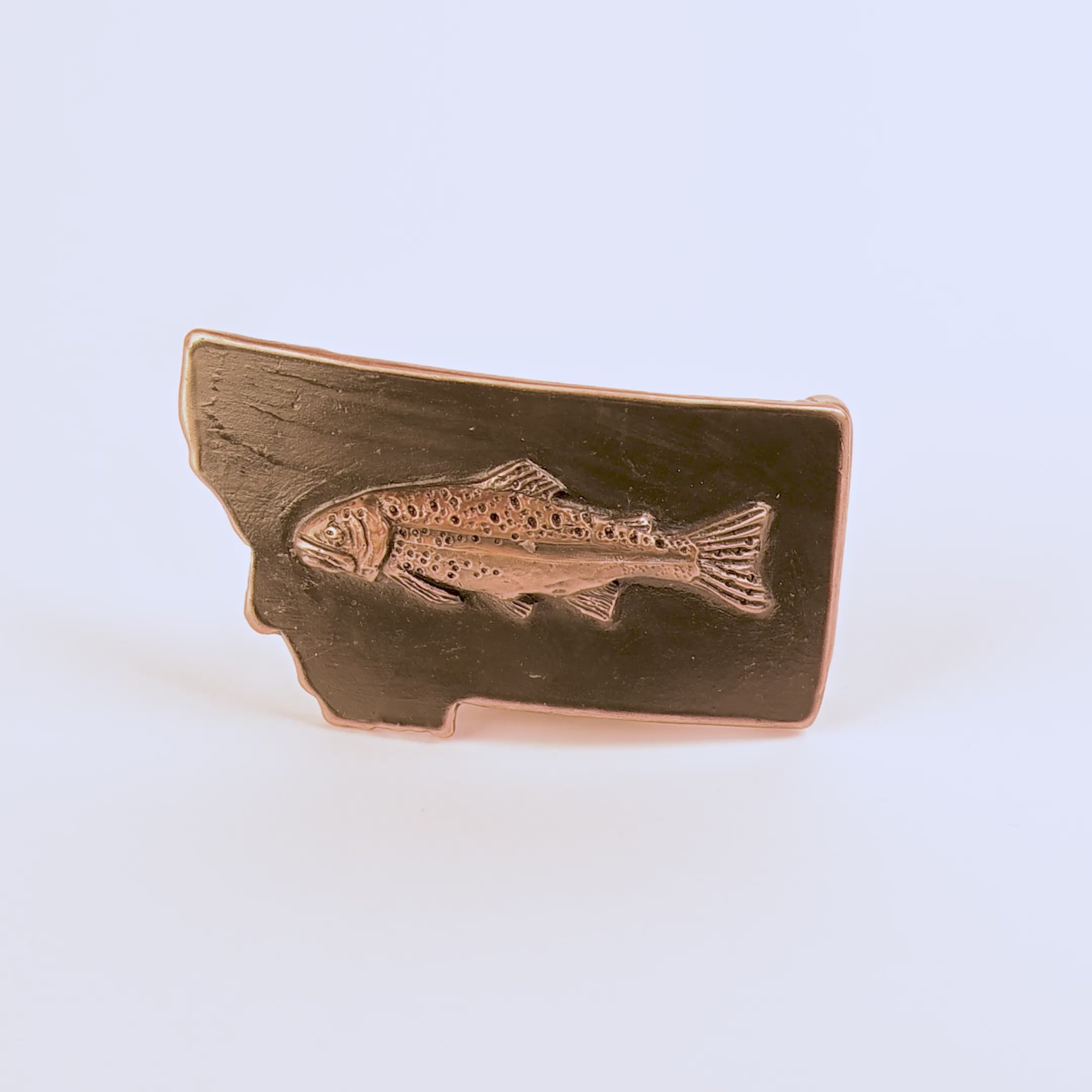 Metallic fish emblem on a black Montana-shaped belt buckle on a white background