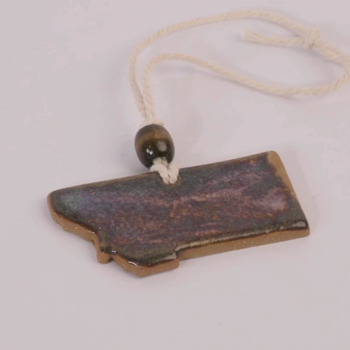 Ceramic pendant shaped like the state of Montana with a bead on a white background