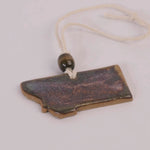 Ceramic pendant shaped like the state of Montana with a bead on a white background