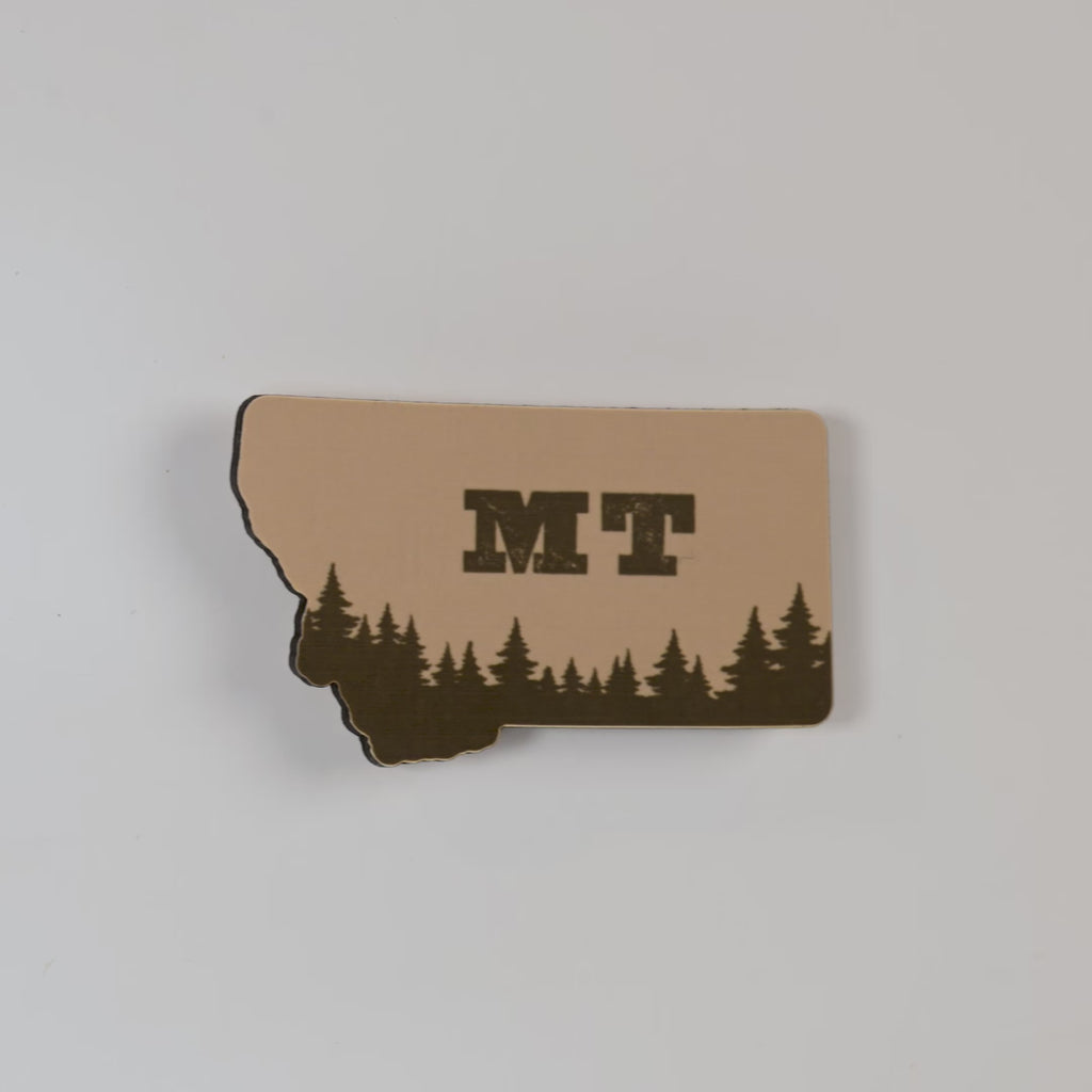magnet of the state of Montana with trees and 'MT' on a white background
