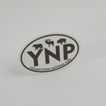 An oval Yellowstone National Park sticker featuring black silhouettes of a bear, moose, and bison above the large letters 'YNP', with 'YELLOWSTONE NATIONAL PARK' curved along the bottom border, shown on a clean white background.