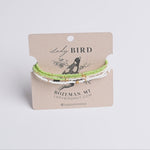 Three beaded bracelets in light green, white, and gold tones displayed on a brown kraft card labeled Lady Bird, photographed against a light neutral background.