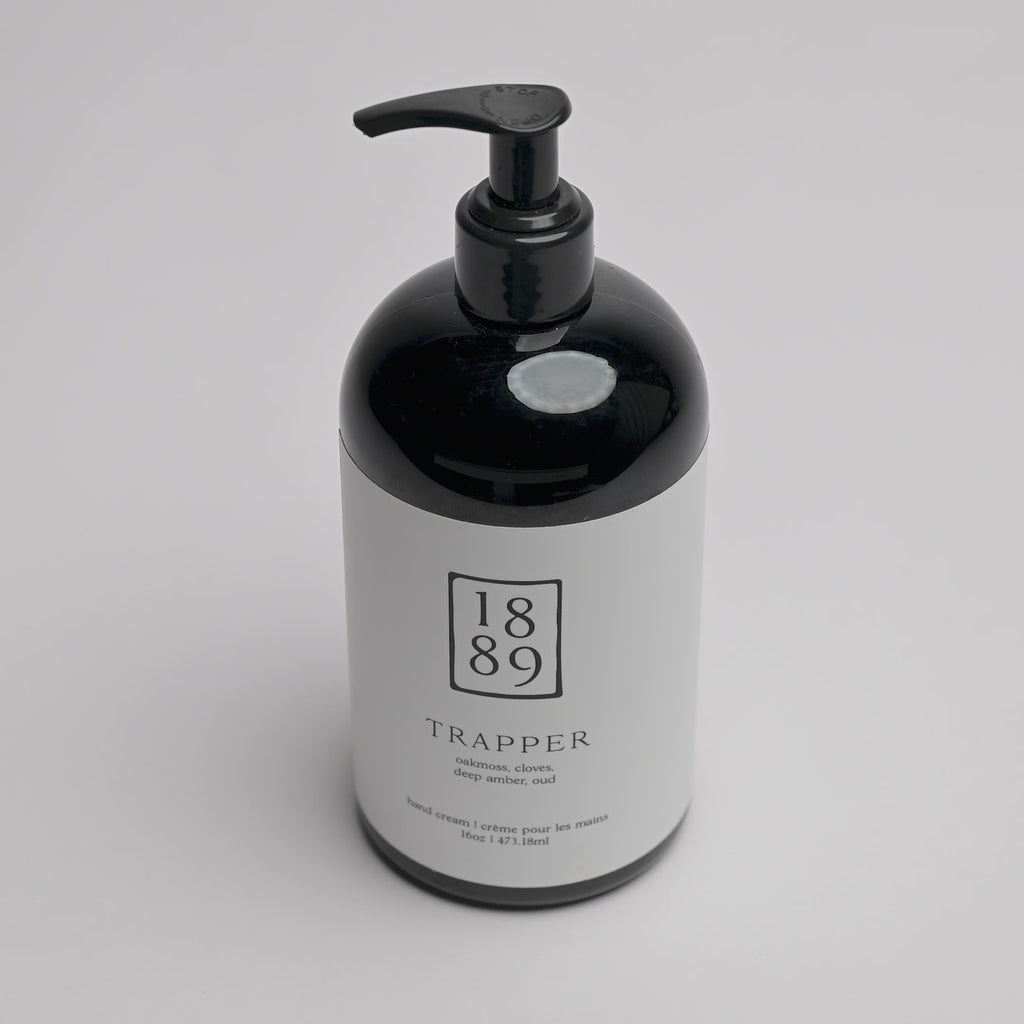 A 1889 brand Trapper hand cream bottle with a glossy black body and pump dispenser, featuring a white label with black text, set against a clean white background.