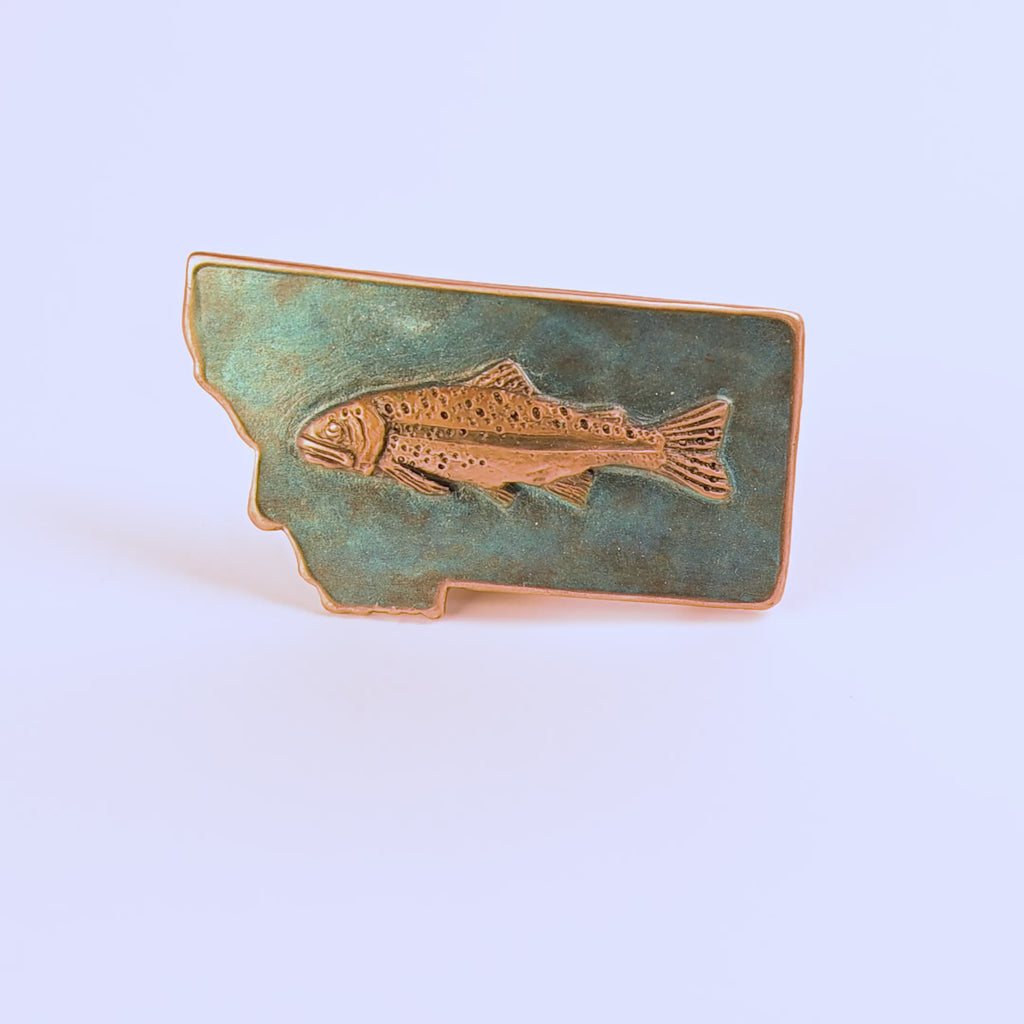 Metallic fish emblem on a blue Montana-shaped belt buckle on a white background