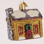 Glass ornament of a cabin with snow on the roof and Christmas decorations on a white background