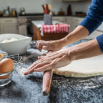 Person rolling dough on a floured surface with kitchen items in the background