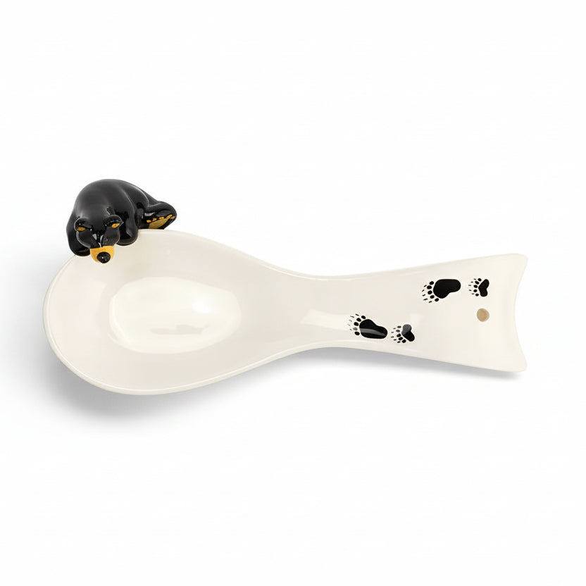 The Bearfoots Bear Spoon Rest by Jeff Fleming features a white ceramic spoon rest with one of Fleming's famous Bearfoots bears perched upon it! 