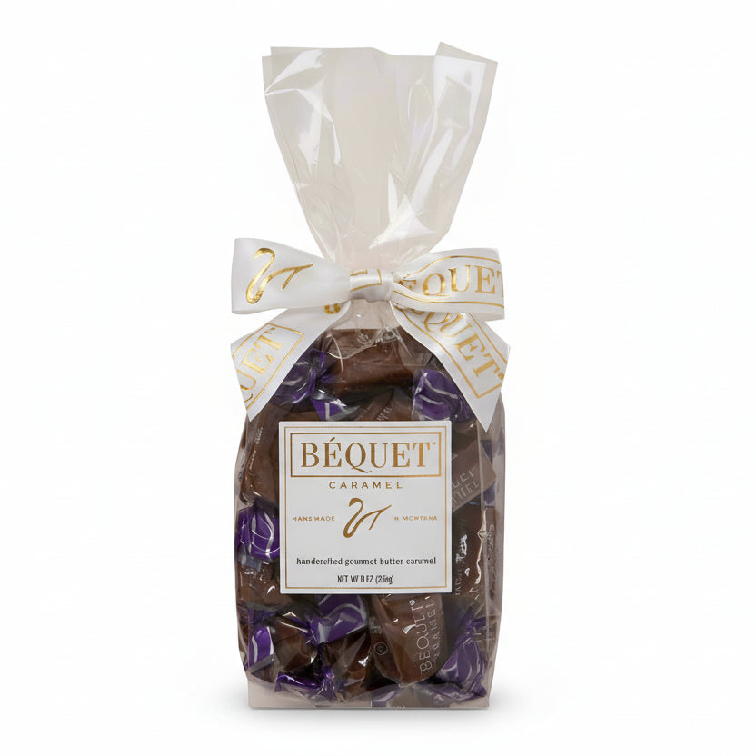 A clear gift bag containing individually wrapped chocolate caramels, with a white ribbon and 'Bequet Caramels' branding on the front.