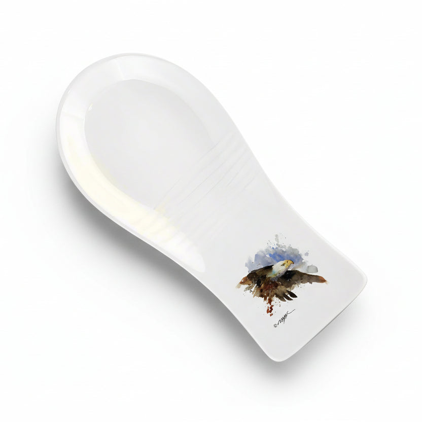 A white stoneware spoon rest with a painted bald eagle in the center.