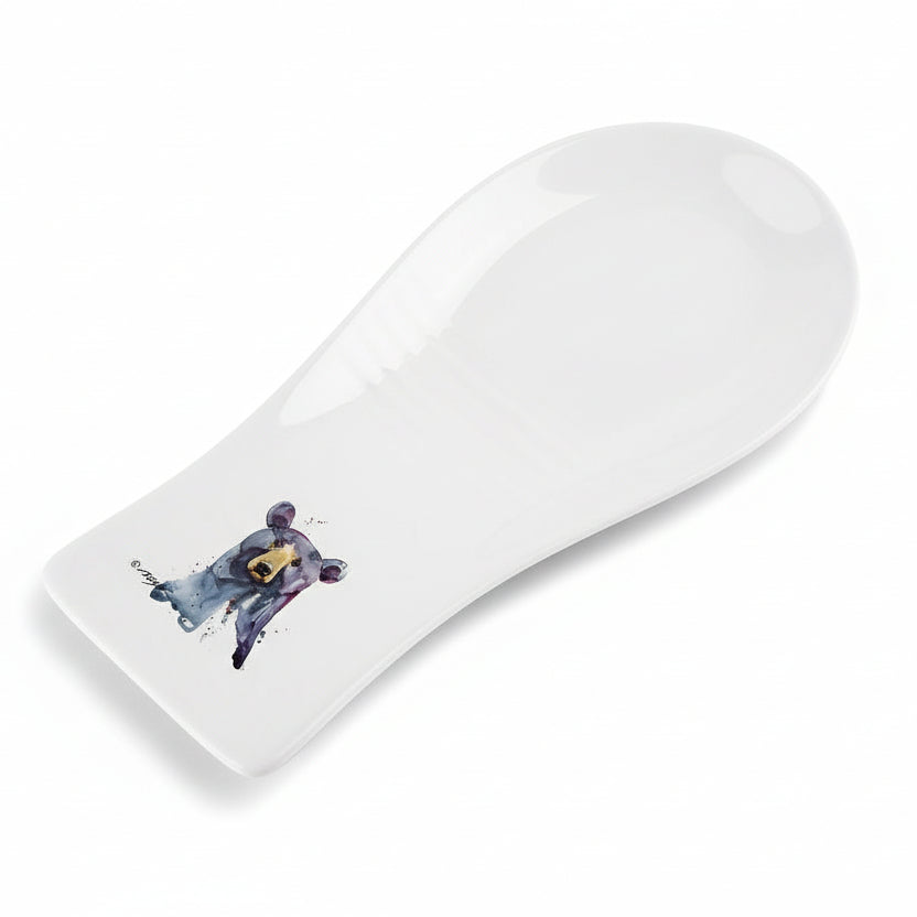 A white stoneware spoon rest with a black bear illustration at the base.