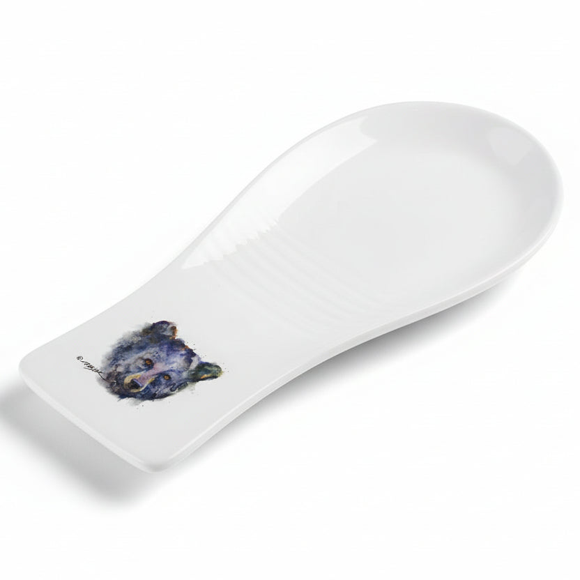 A white stoneware spoon rest with a painted bear's face in the lower right corner.