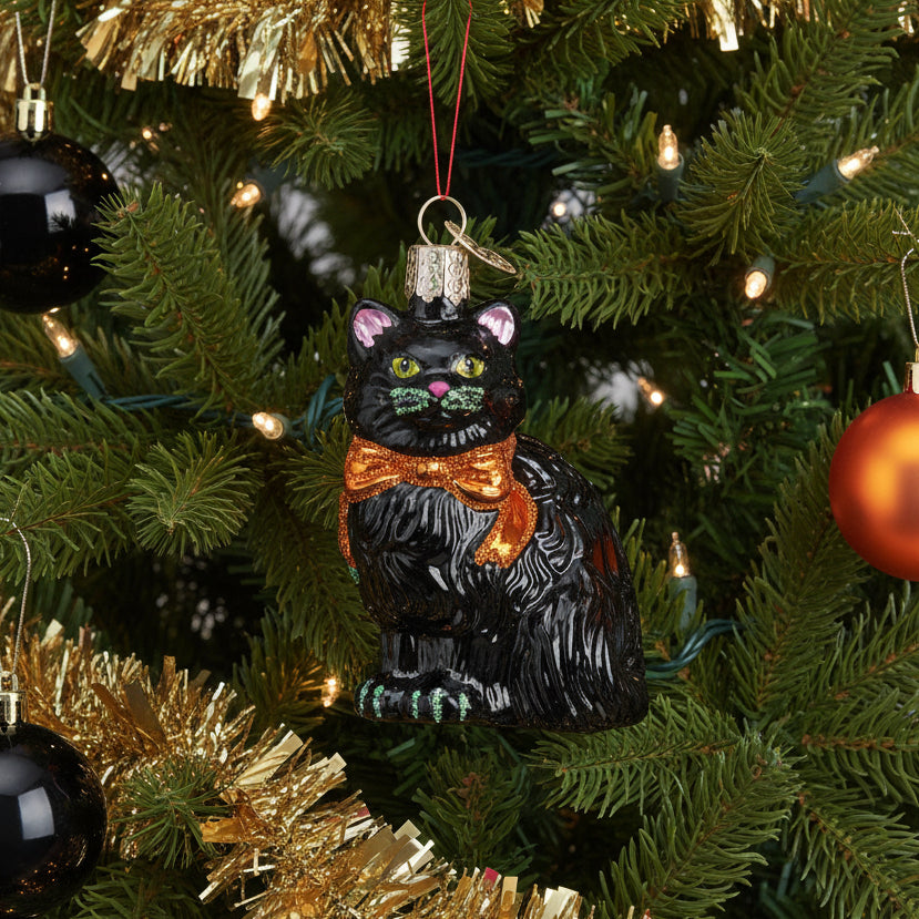 Glass ornament of a black cat with a gold bow tie on a white background