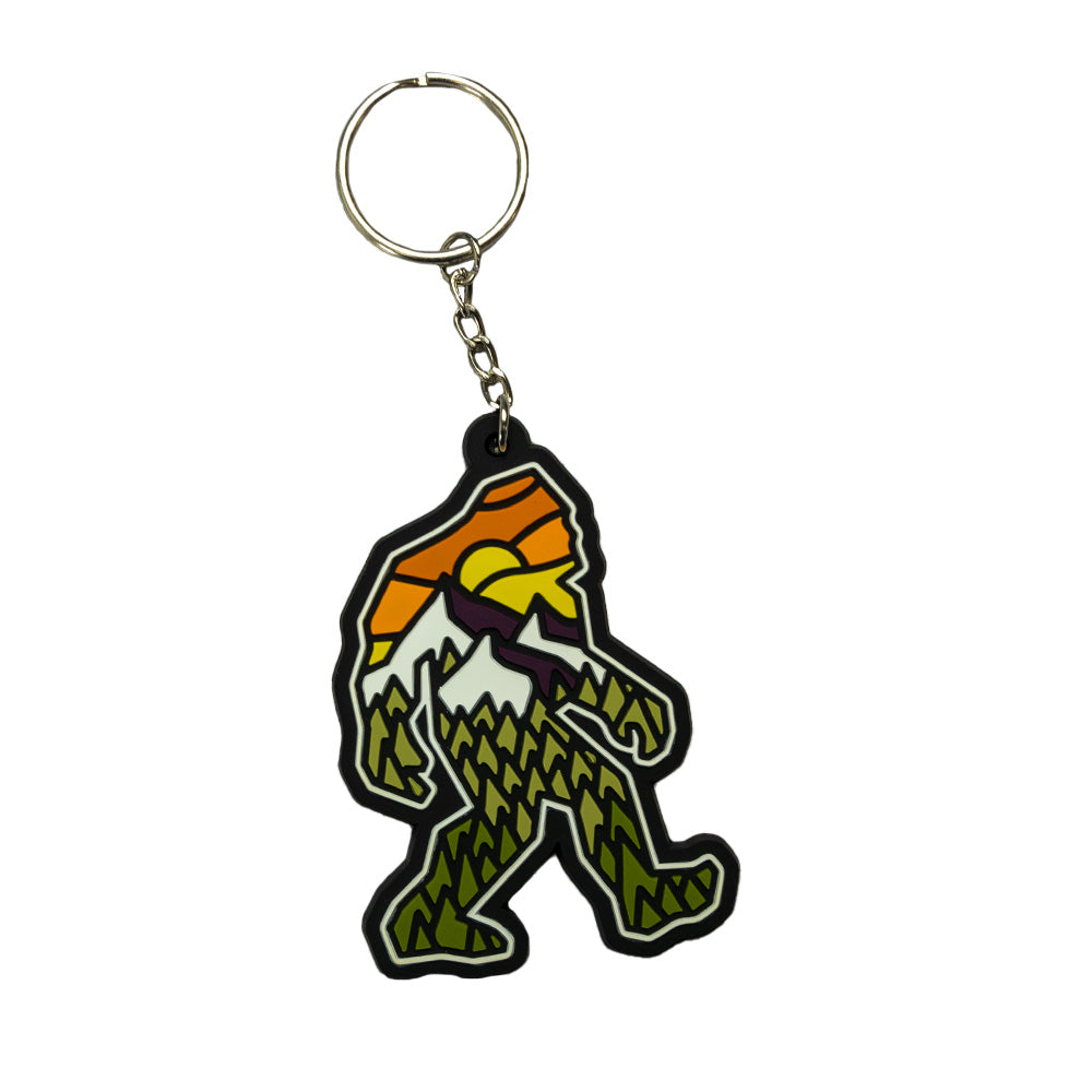 keychain shaped like a yeti with a sunset design over a mountain view and a forest
