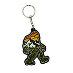 keychain shaped like a yeti with a sunset design over a mountain view and a forest