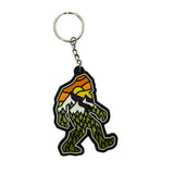 keychain shaped like a yeti with a sunset design over a mountain view and a forest