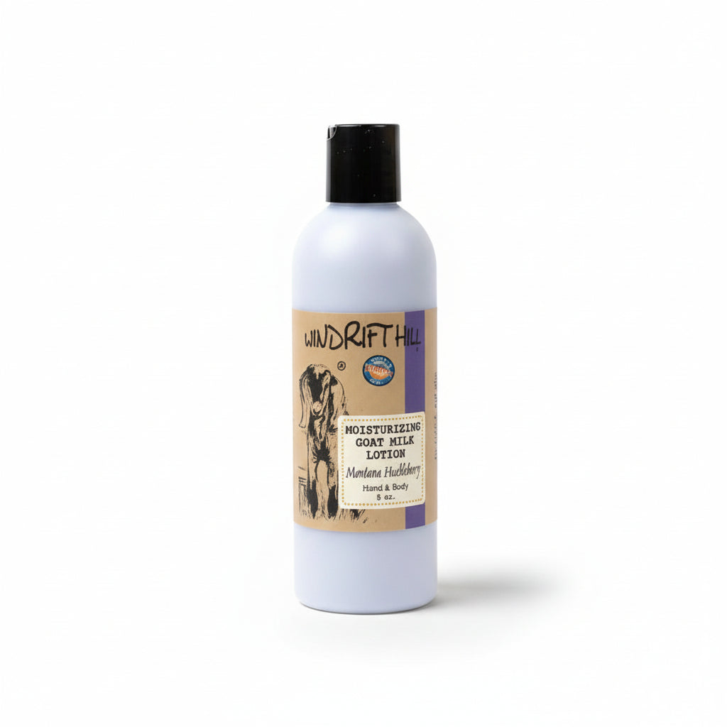 A white bottle of Montana Huckleberry Goat's Milk Lotion by Windrift Hill, with a label featuring a huckleberry and goat illustration, placed against a neutral background.